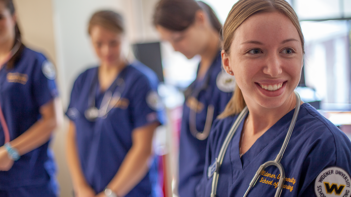 BSN degree nursing student in clinical lab smiling with classmates in the background