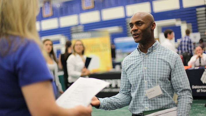 Student at career fair 710x400 Student at Widener career fair talking through resume with prospective employer