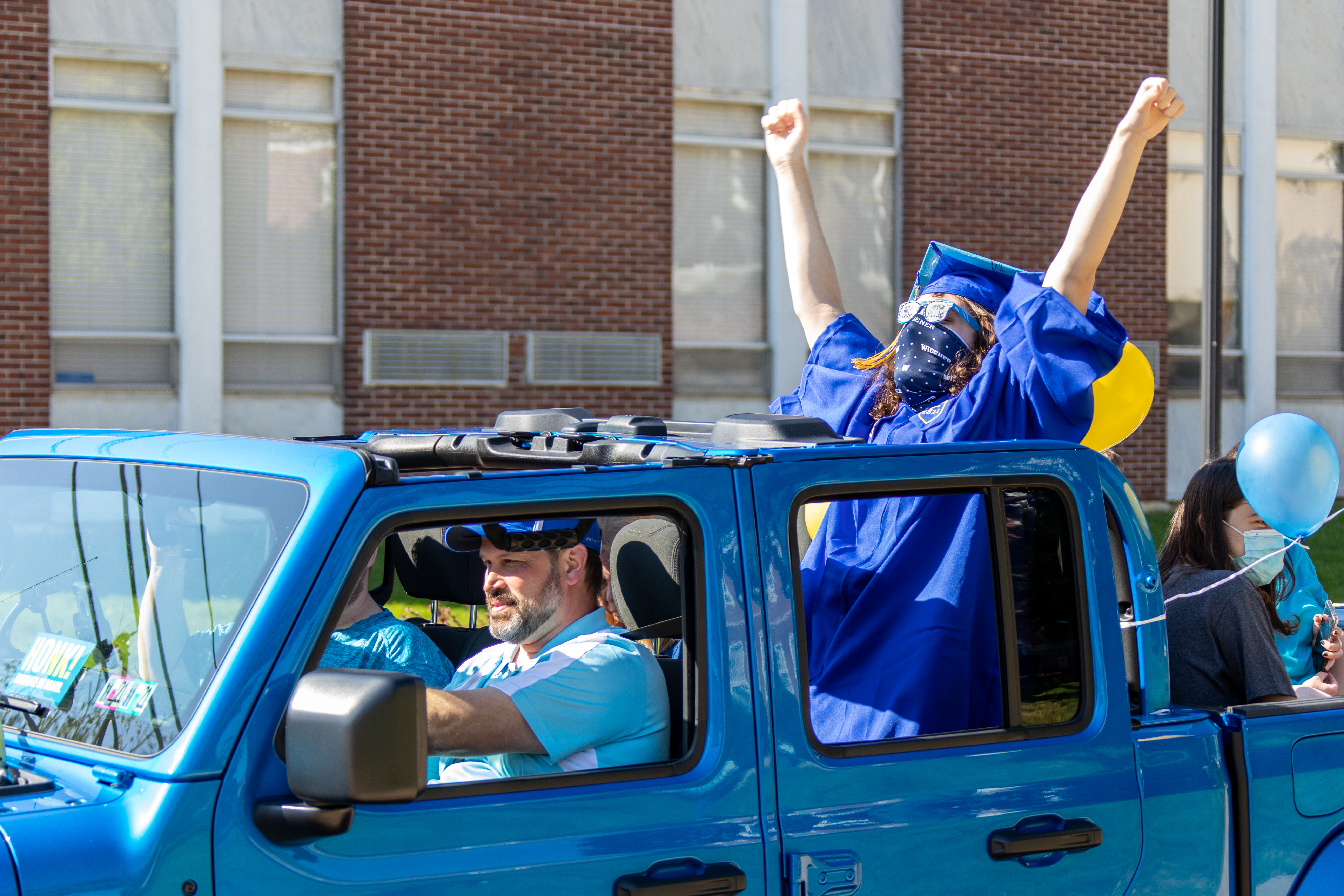 Graduate puts arms in the air while in the back of a blue vehicle