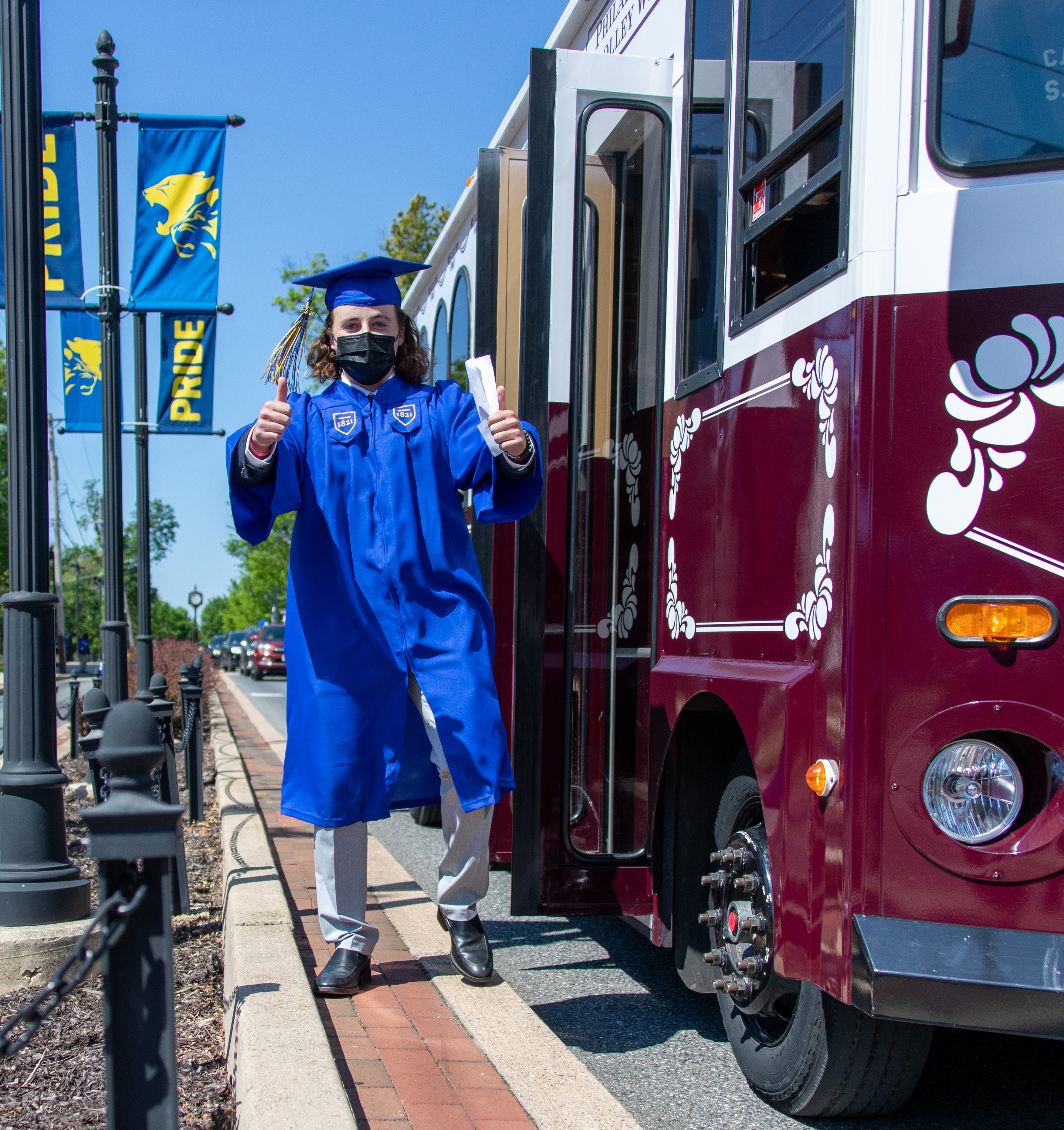 Graduate in cap and gown gives thumbs up in front of trolley