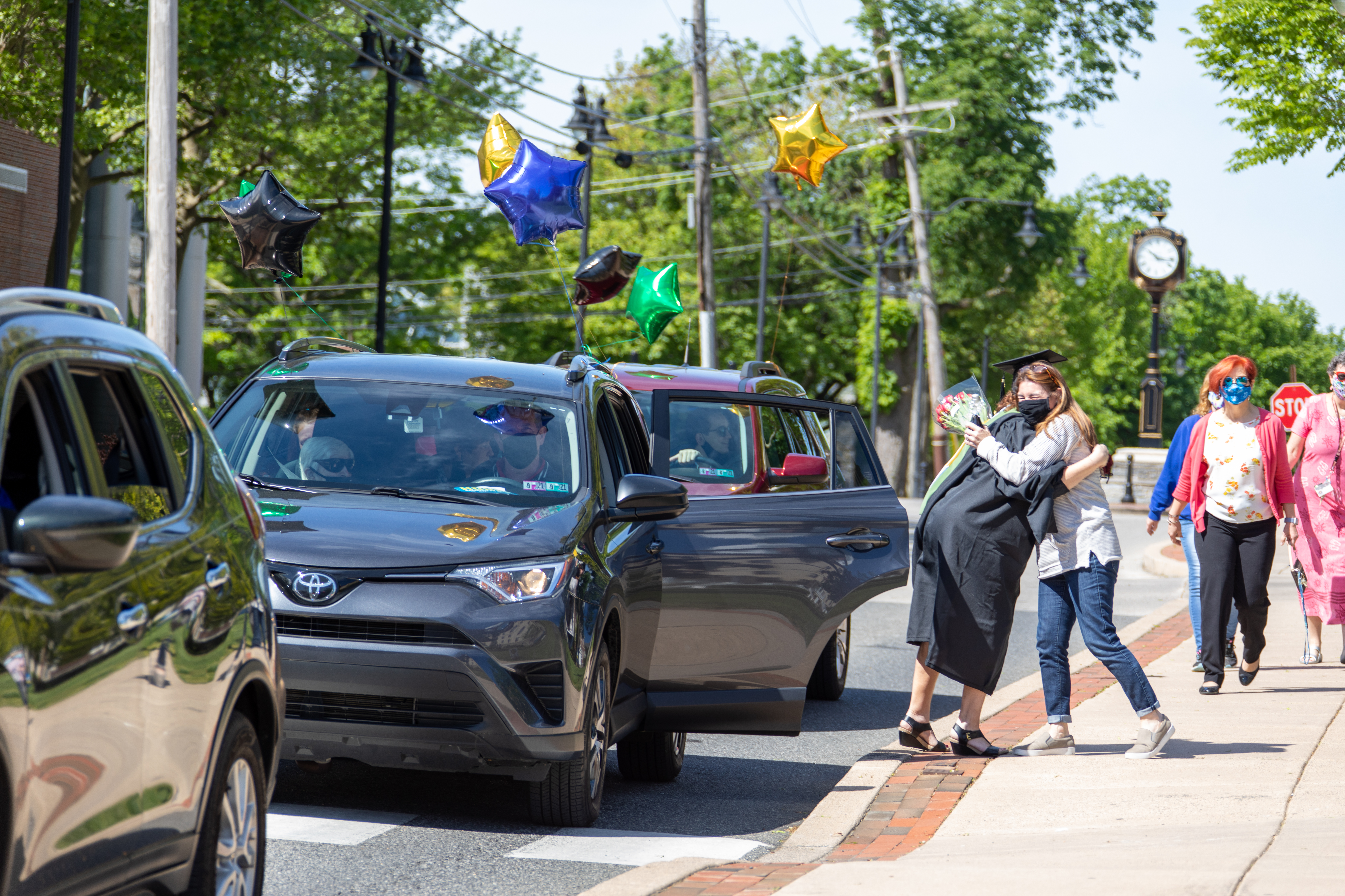 Graduate and person hug next to car