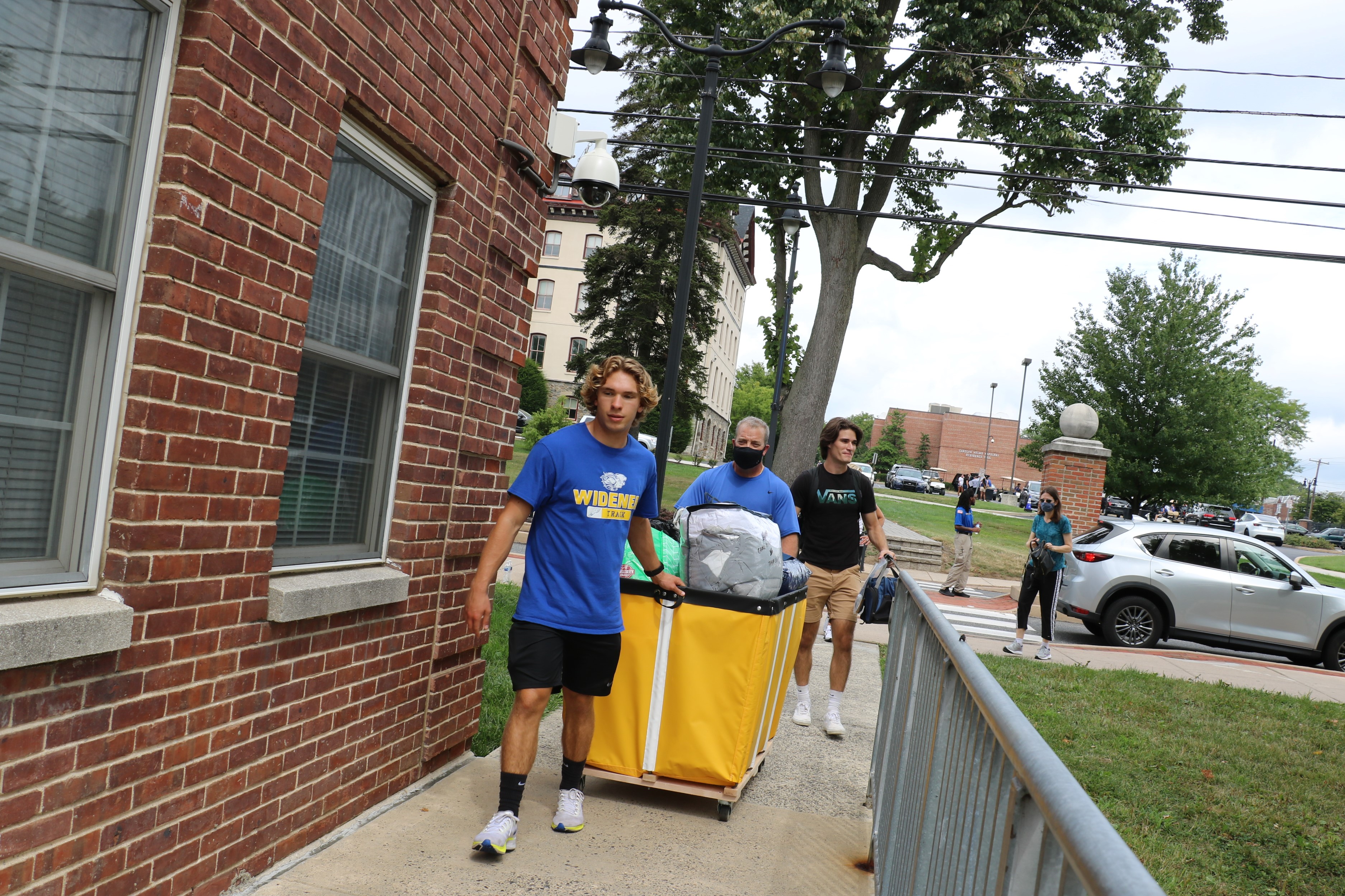 Student volunteers push a luggage bin to help an incoming student move in.