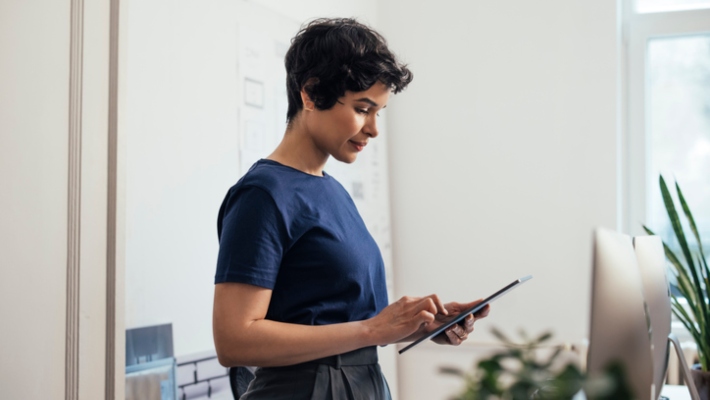 Business professional in home office standing and looking at a tablet