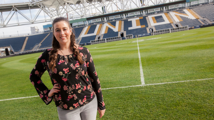A Widener University student who interns with the Philadelphia Union stands in front of the soccer field.