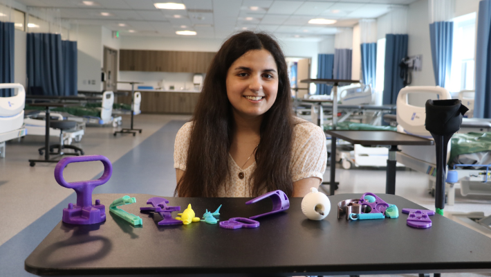 Lydia Aruffo sits at a table, smiling, with all of her 3D printed devices