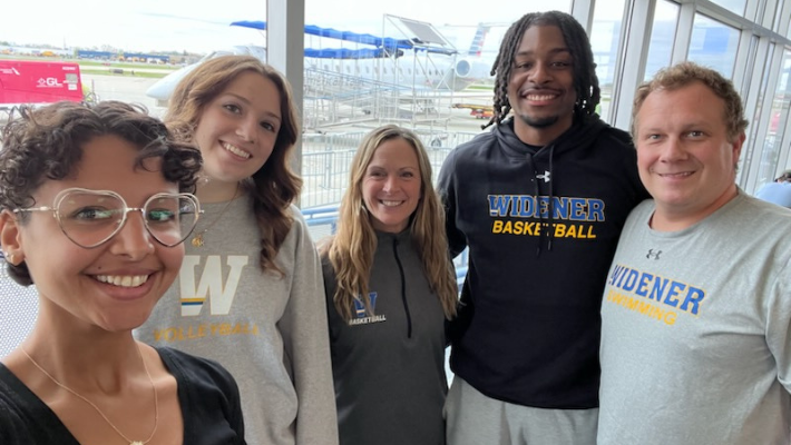 The group of student athletes and athletic staff pose for a photo at the airport before their conference trip