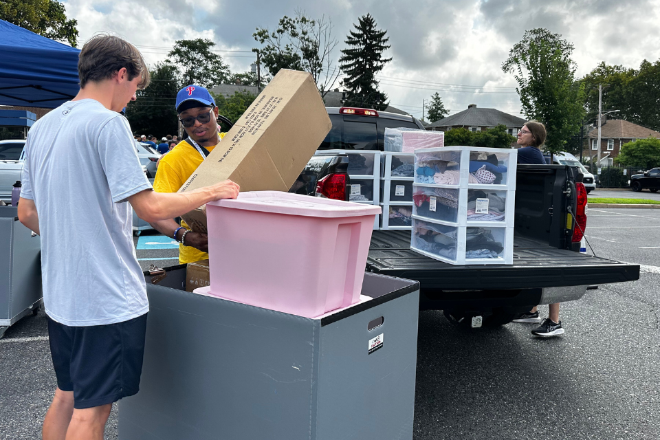 Student volunteers unload belongings from a pickup truck and place them in a rolling cart.