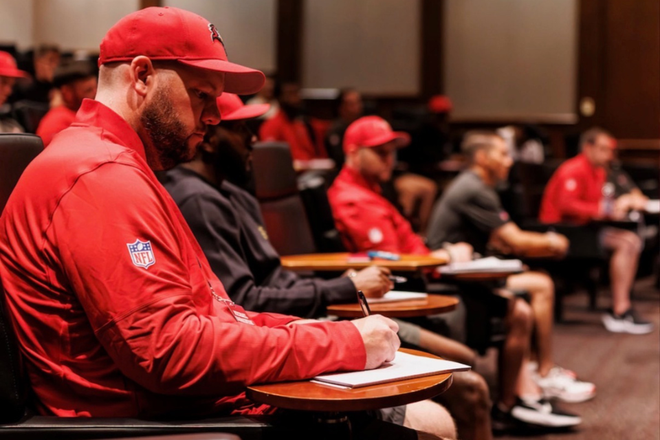 Mike Barainyak and other attendees sit at desks and take notes during a session