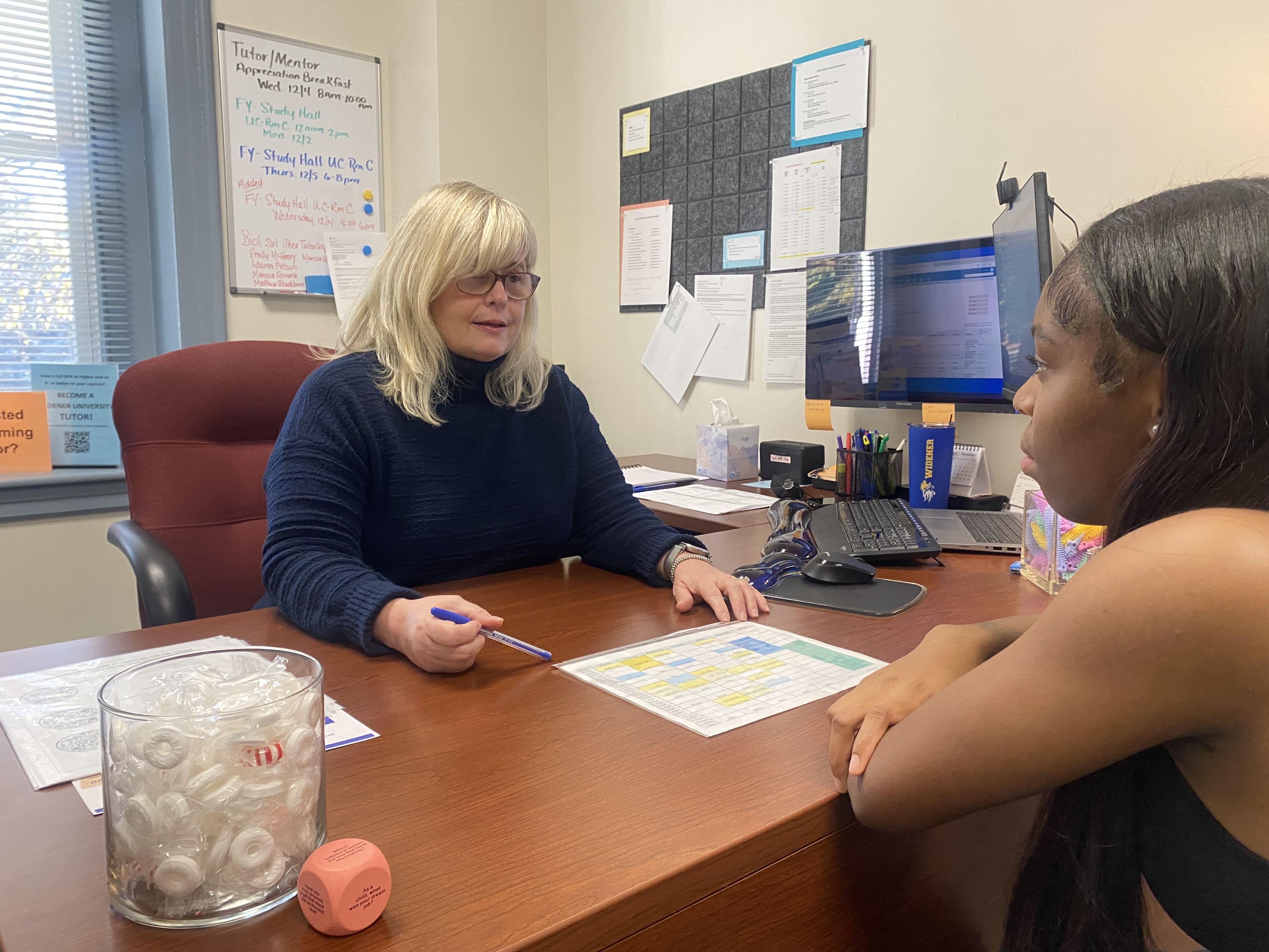 Academic coach talks with a student at her desk.