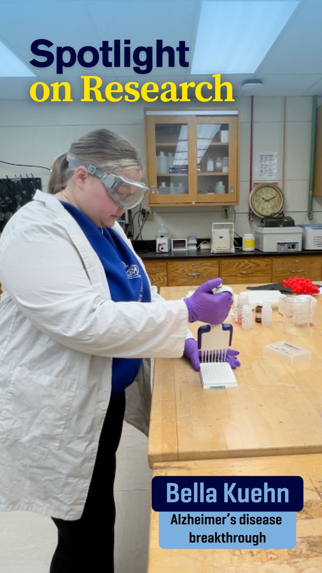 Bella Kuehn wears goggles, a lab coat, and gloves while working in the lab.