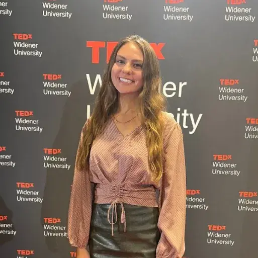 Natalie Sassi poses in front the TEDxWidenerUniversity banner after giving a talk on stage.