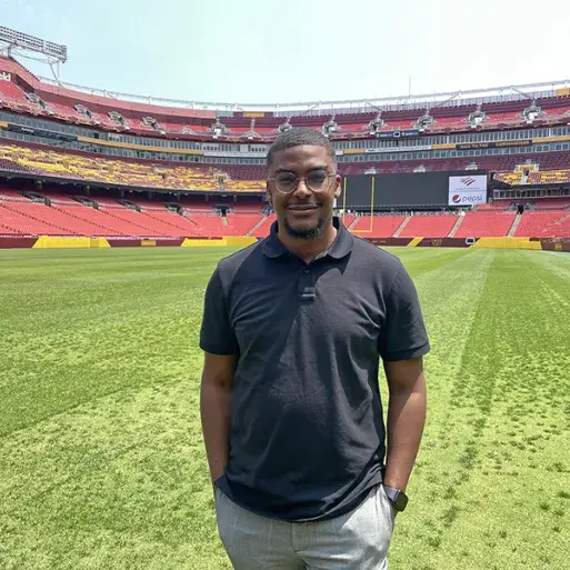 Alumnus Andrew Proctor stands on the field at the Washington Commanders football stadium