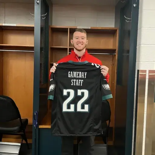 Tiernan poses holding a Philadelphia Eagles jersey that reads "gameday staff"