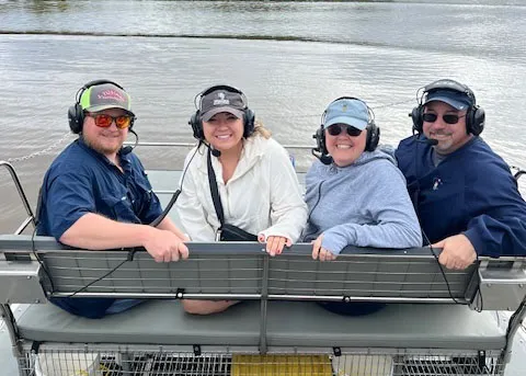 Four people face the camera smiling on a boat in the water