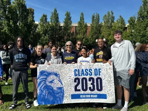 Students pose for a photo with President Robertson holding the "Class of 2030" banner signed by new students 