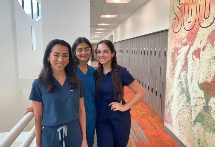 Three female PA students in scrubs stand together for a photo.