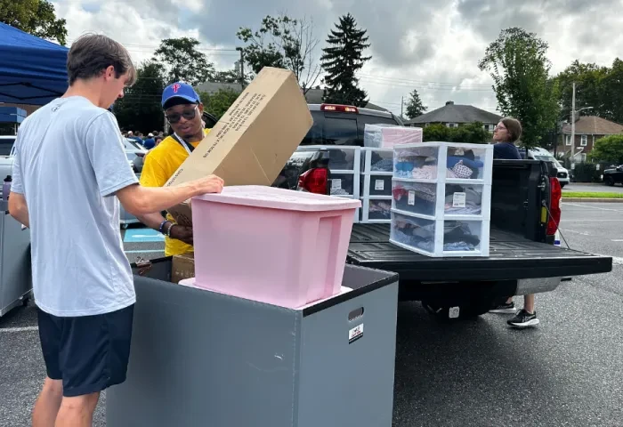 Student volunteers unload belongings from a pickup truck and place them in a rolling cart.