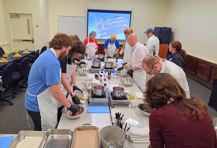 Students and staff stand around a long table with bowls and burners cooking a dish