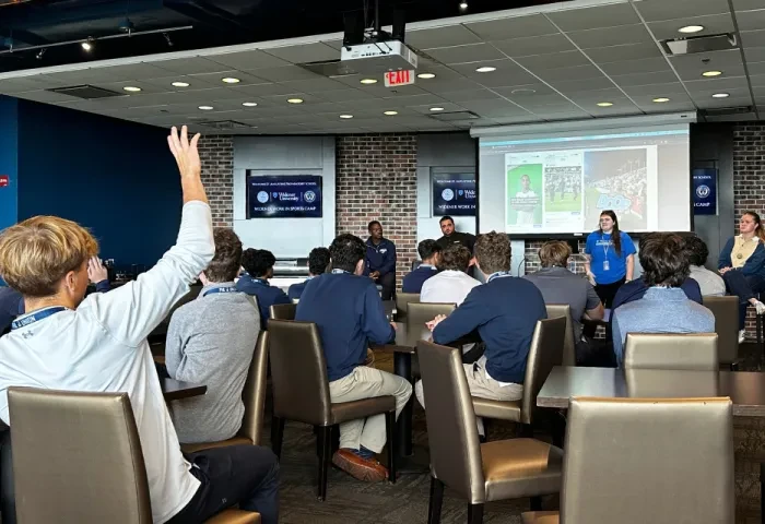 A student raises their hand with a question at a presentation.
