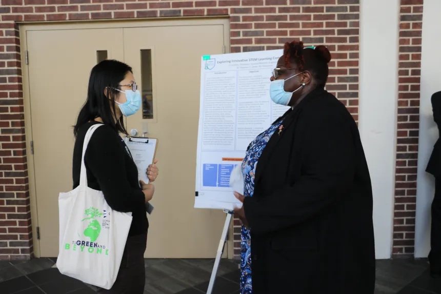 A female student present their poster to a female symposium attendant.