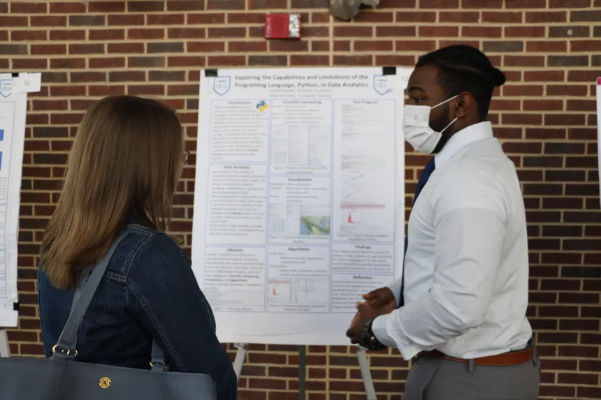 A male student presents their poster to a female symposium attendants.