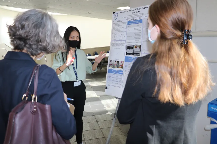 A female student presents their poster to symposium attendants.