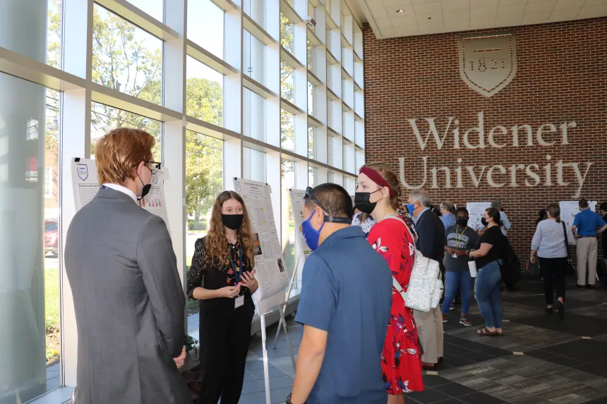 A female and male student present their poster to symposium attendants.