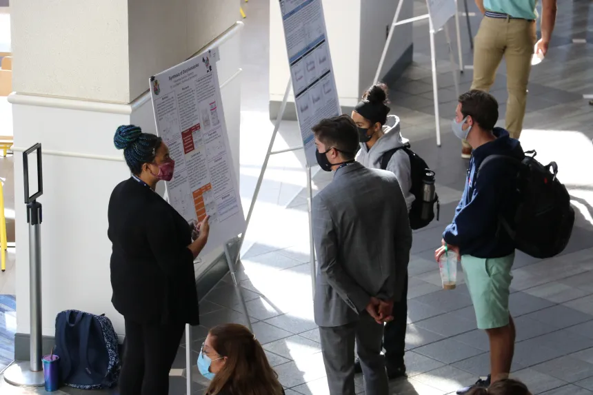 A female student presents their poster to symposium attendants.