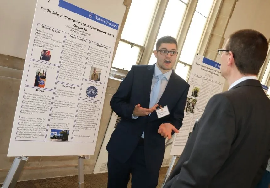 A male student presents his research poster at the HIP Fair