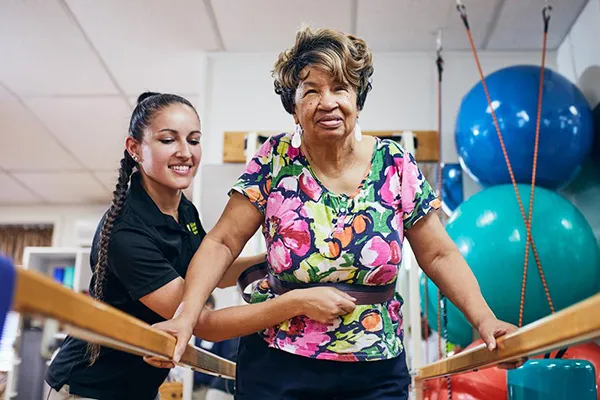 Physical therapy student works with a client, walking between the parallel bars