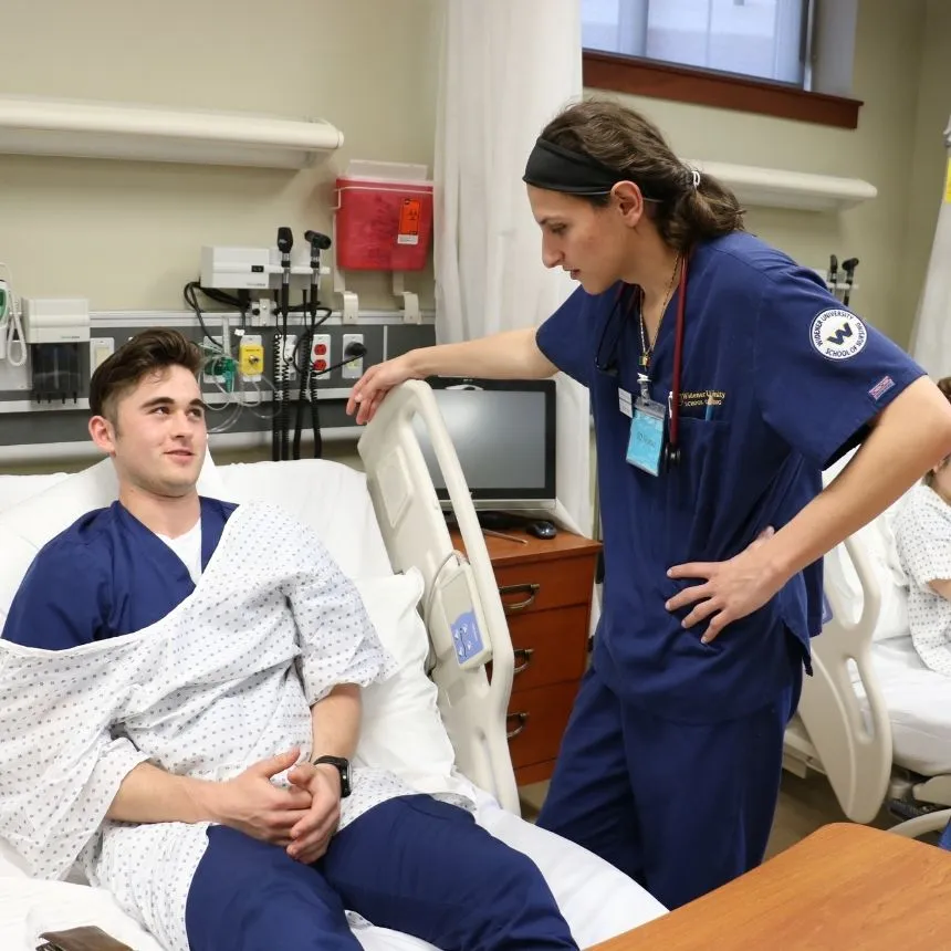 A male nurse tends to a patient in a bed in the simulation center