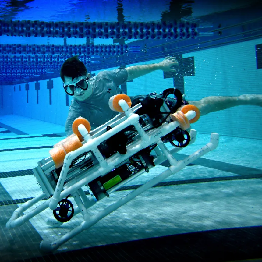 A male students swims underwater next to the robosub