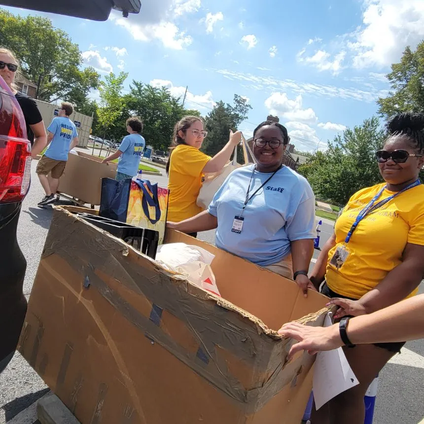 Female student volunteers smile while unloading a car.
