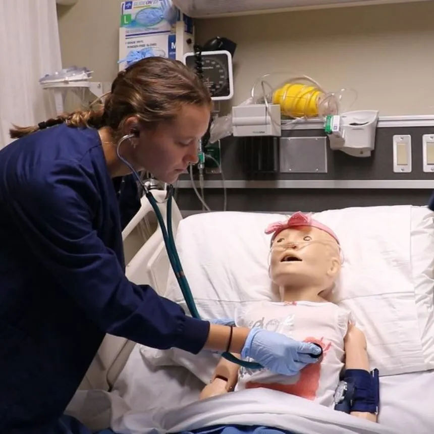 A female nursing student listens to a heartbeat on a pediatric mannequin.