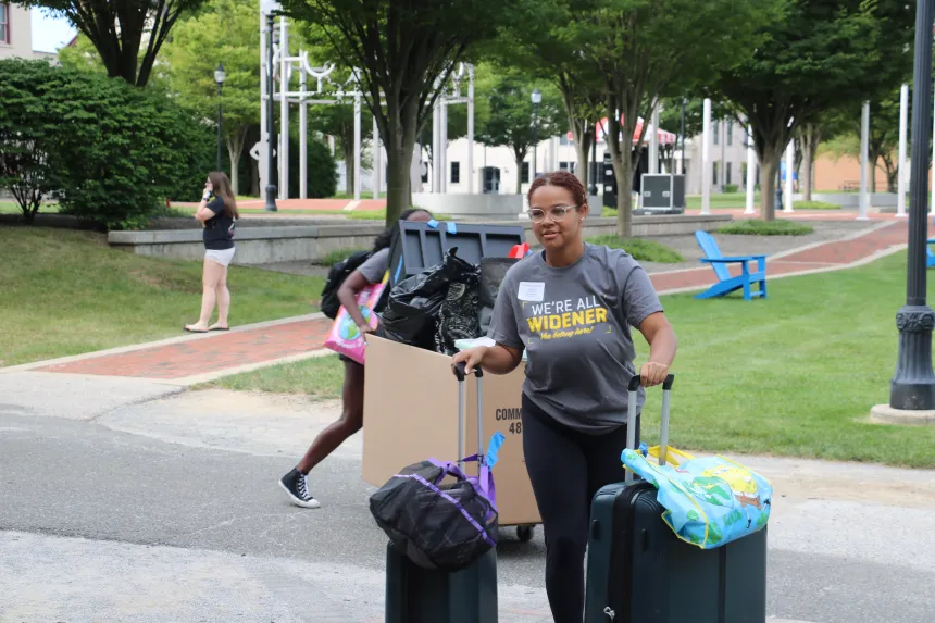 A student wearing a "We're all Widener" shirt rolling suitcases