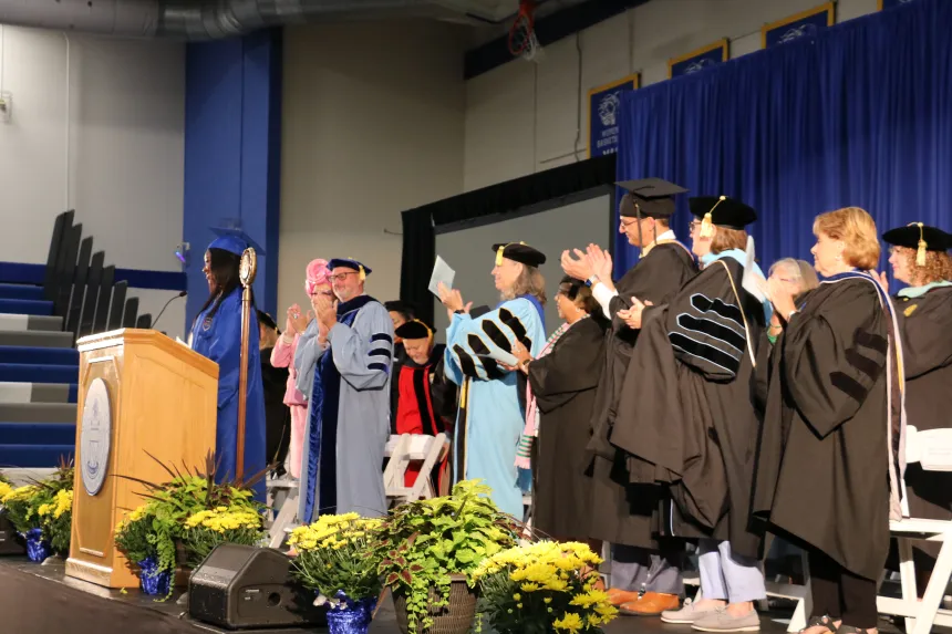 Faculty and staff on stage in academic regalia cheering