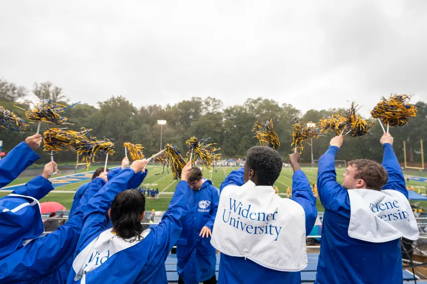 Students in the stands cheer with pom poms wearing Widener University jackets