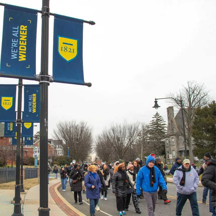Peace march participants walk under a We're All Widener banner on campus.