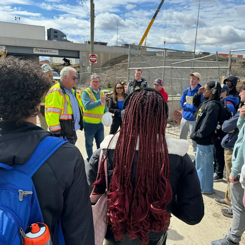 Students stand at the construction site and listen to a project overview from Robert Buckley