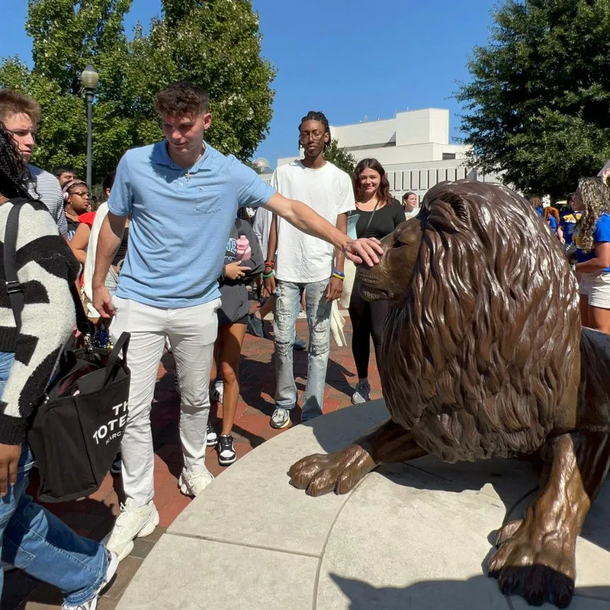 A male student rubs the lion's nose at the Pride statue.