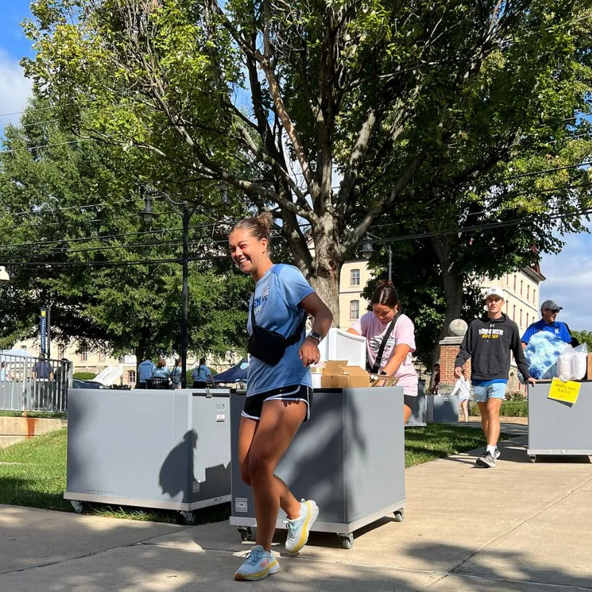 Female students roll bins to help students move in.