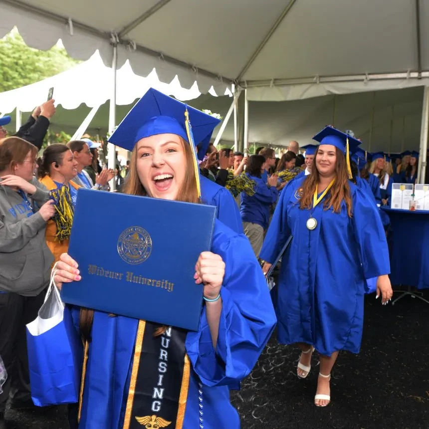 A female graduate smiles with her diploma during the recessional.