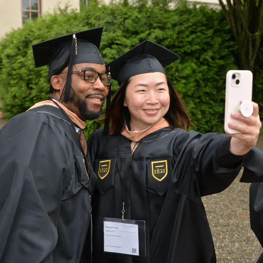 Male and female grad students take a selfie together at commencement.