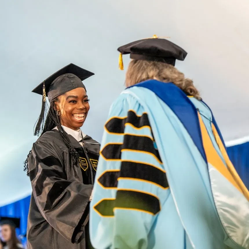 A female graduate shakes the president's hand on stage at commencement.