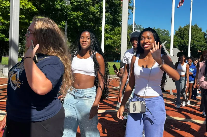 New students walk under the dome and wave at the camera, smiling.