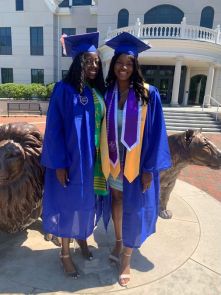 Ricki and Priscilla pose in front of the Pride statue in their cap and gowns.