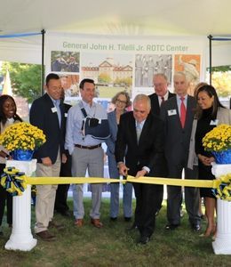 Gen. Tilelli stands in front a mural and cuts a ribbon with members of the board of trustees behind him.