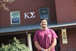 Willie Mathis III stands in front of his fraternity house Kappa Sigma that displays the chapter's Greek letters.