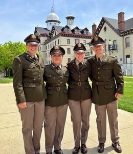 Four ROTC students commissioned as Army officers standing outdoors with Old Main behind them.