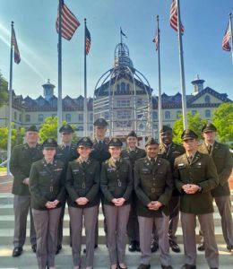 ROTC cadets stand in uniform in front of Old Main and American flags.